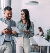 Shot of a two confident business persons talking in the work place. Two colleagues using a digital tablet while walking in a modern office. Businessman and businesswoman in meeting discussing business strategy. Business coworkers working together in the offic